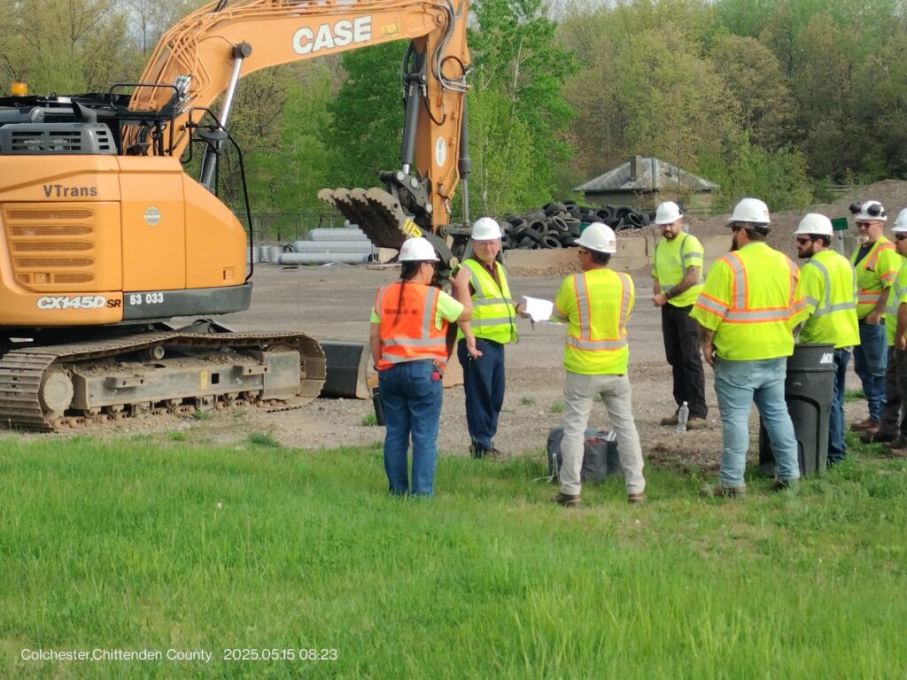 five men in hard hats standing outside near an excavator